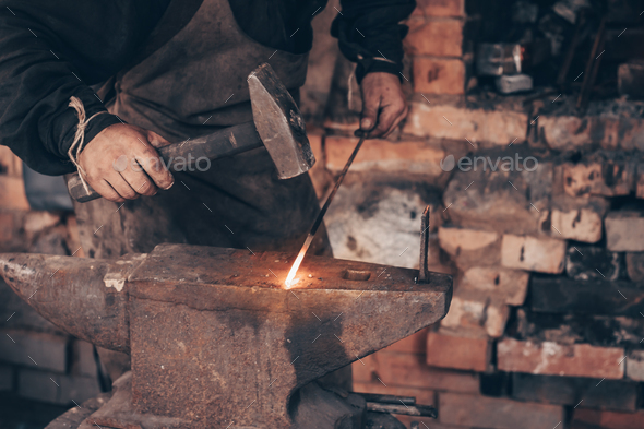 Blacksmith process glowing metal with hammer on anvil in forge. Dirty hands of farrier strike iron