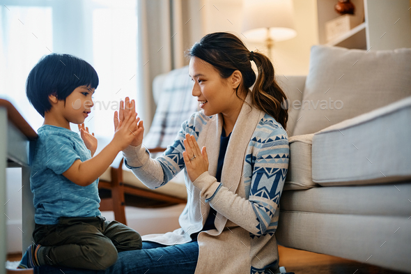 Happy Asian mother and son playing clapping game at home.