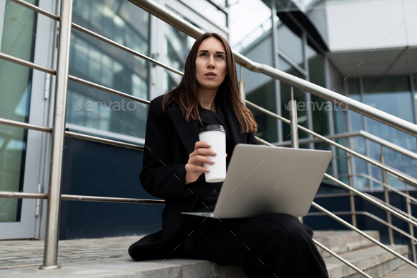 female market risk analyst working with laptop outside office building, reporting concept