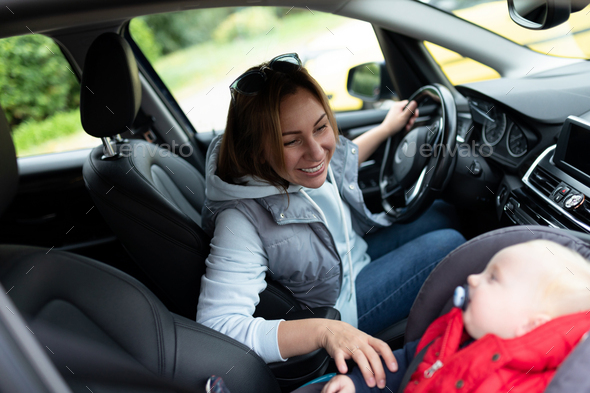 a young mother driving a car looks at a baby in a carrier in the front seat