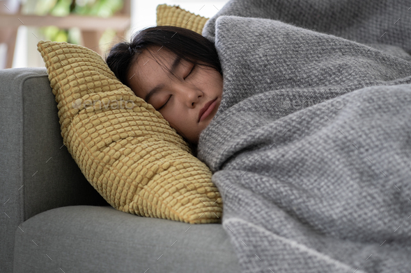 Calm Asian young woman peacefully lying relaxing resting on cozy couch sleeping taking nap at home.