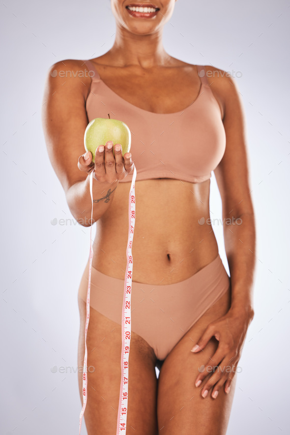 Black woman, apple and measure tape for diet, wellness and healthy lifestyle with lady on grey stud