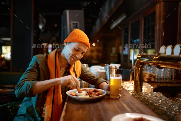 Young man football fan eating snack and drinking beer in sports bar