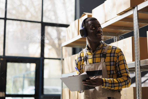 African american storehouse employee in headphones supervising warehouse merchandise - Stock Photo - Images