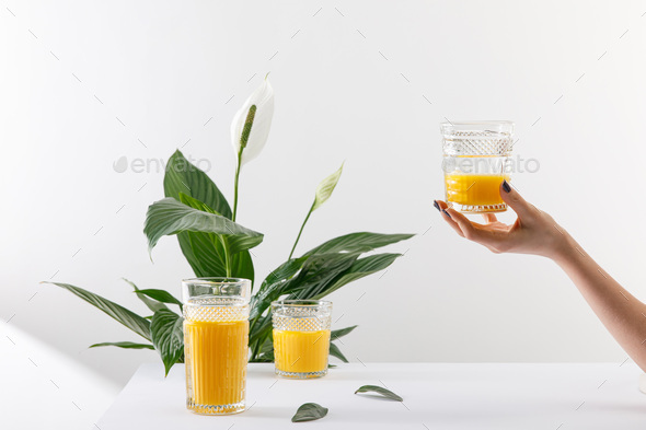 cropped view of woman holding glass of fresh delicious yellow smoothie near green peace lily plant