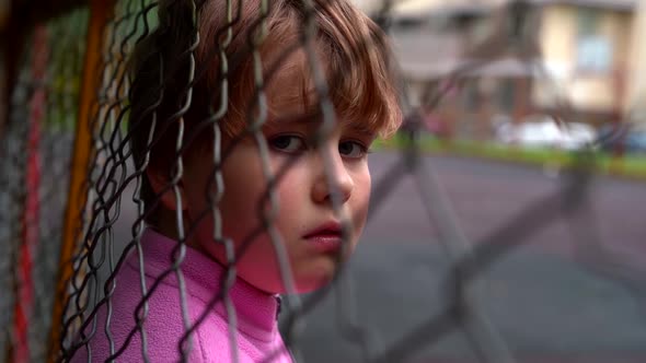 Unhappy Lost Child Behind Grid in Outskirts of City, Portrait Shot alt