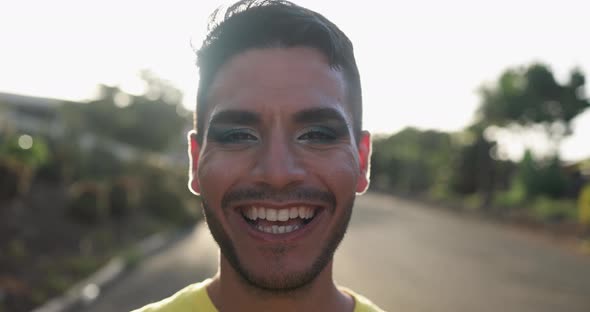 Young happy transgender man with makeup smiling on camera with sunset in the background alt