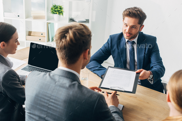 Selective focus of employee in formal wear holding resume near recruiters at table