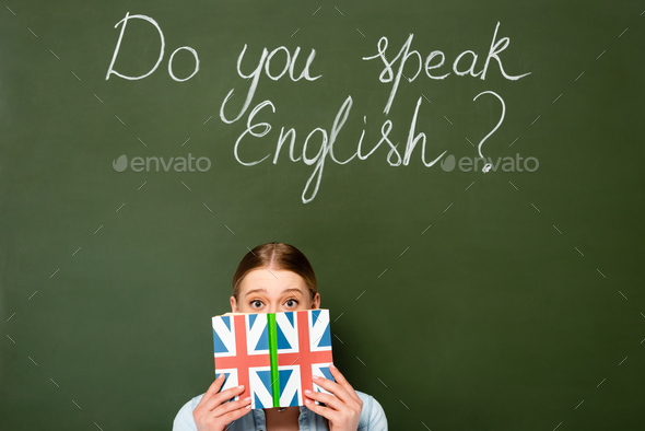 pretty girl with obscure face holding book with uk flag near chalkboard with do you speak English