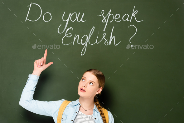 girl with backpack pointing at chalkboard with do you speak English lettering