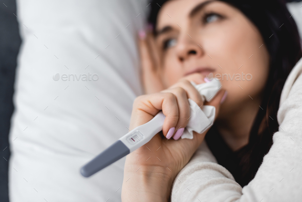 selective focus of sad woman holding pregnancy test with negative result and tissue