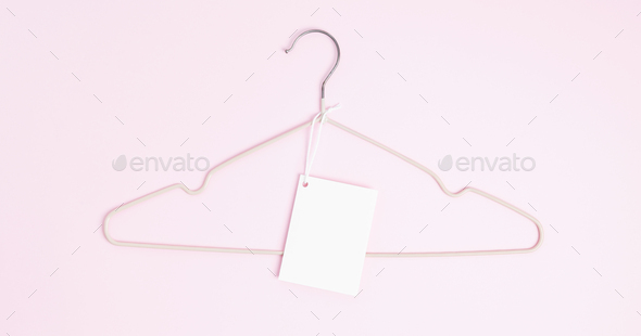 Creative flat lay hanger with white paper label pink background. Clothing tag, label blank mockup