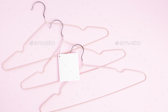Creative flat lay hangers with white paper label pink background. Clothing tag, label blank mockup