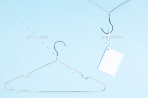 Creative flat lay hanger with white paper label blue background. Clothing tag, label blank mockup