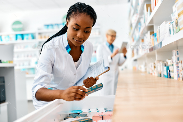 Young black pharmacist looking for medicine while working in drugstore.