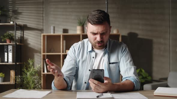 Young Man Using Cellphone Software Applications Sitting at Table Feeling Dissatisfied Irritated By alt