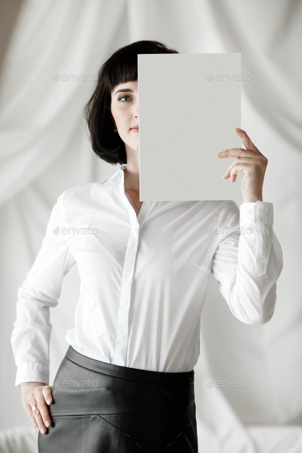 beautiful young woman with dark short hair holding a magazine, book with mock up. girl in a white