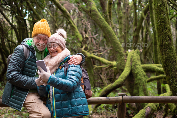 Smiling senior couple enjoying nature outdoors in mountain forest with moss covered trunks