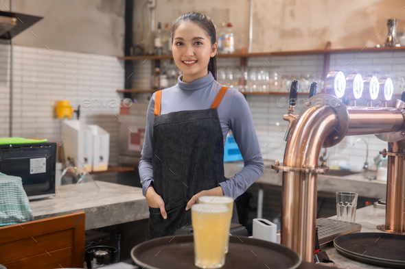 Portrait of Asian bartender girl hand at beer tap pouring , waitress or staff serve and craft