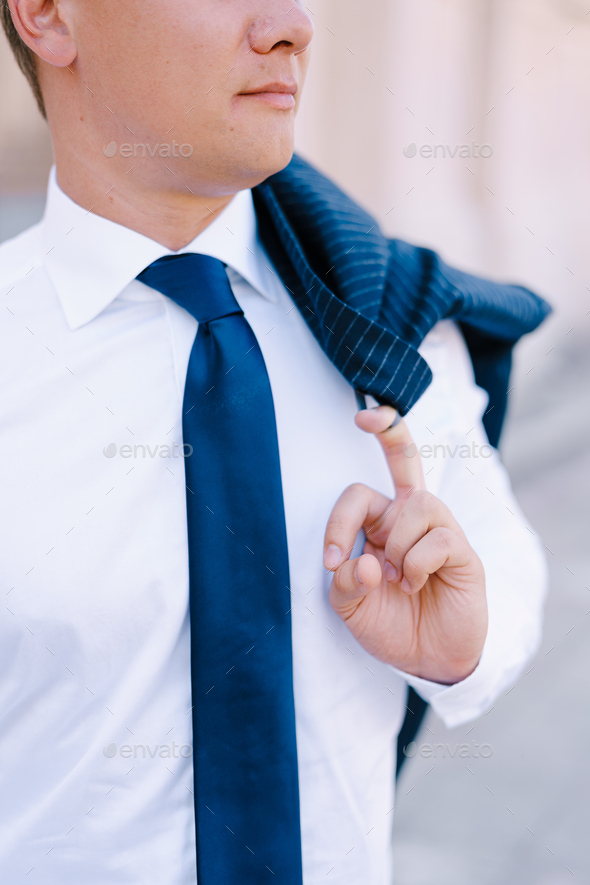 Man in a white shirt holds a jacket hanging on his shoulder with his finger