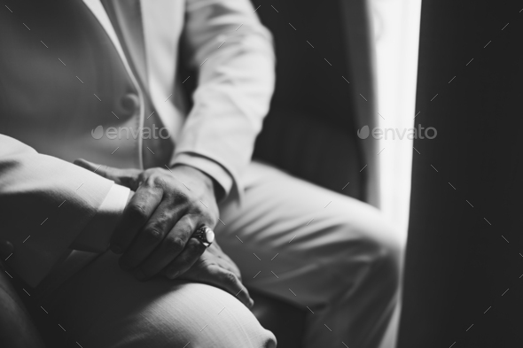 A man in a suit with a signet ring on his little finger sits by the window, close-up, black and