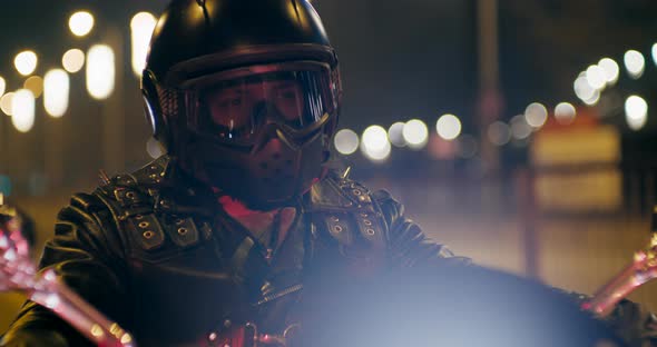Male Rock Biker in Black Helmet Waits on Lights on Motorcycle at Night in City