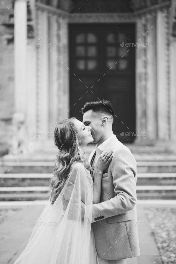 Groom hugs and kisses bride against the background of the entrance to the Basilica of Santa Maria