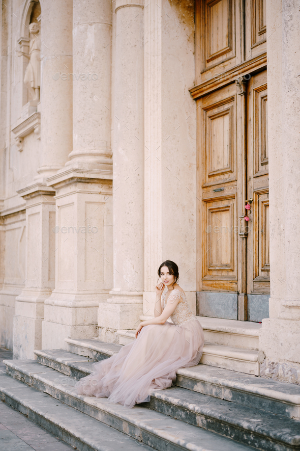 Bride sits on the steps of an old building in front of the entrance