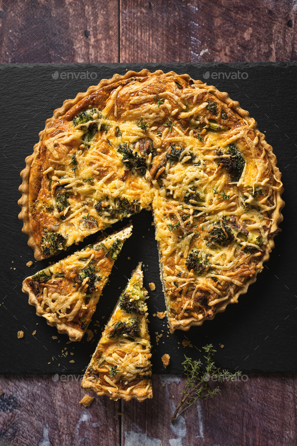 Top down view of a delicious broccoli quiche on black slate background on wooden table - Stock Photo - Images