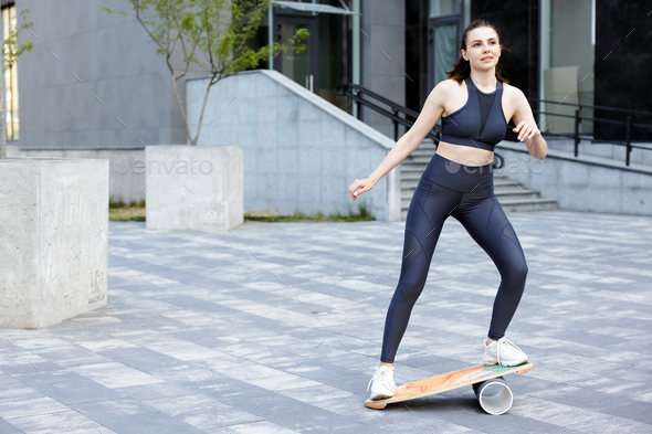 Female athlete trying to keep balance, while training on balance board in city.