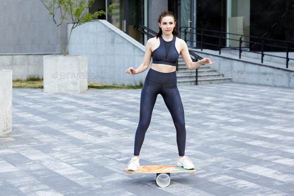 Smiling female trainer in activewear practicing on balance board in town.