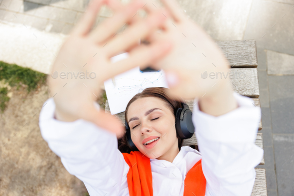 Relaxed woman enjoying music, while lying down on bench.