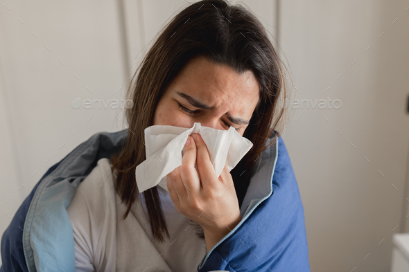 Young ill woman sneezing into a tissue