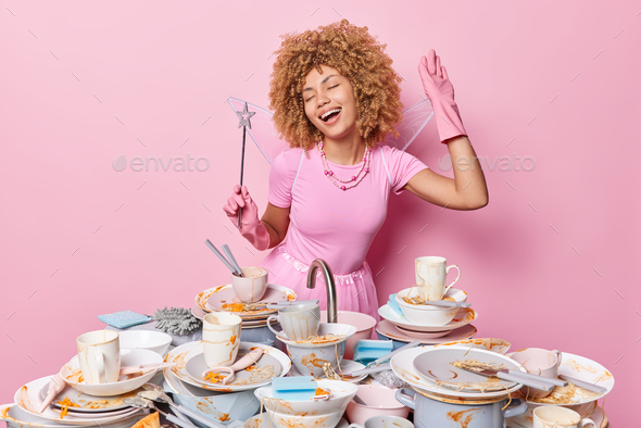 Cheerful female fairy holds magic wand dreams about wishes come true sings along stands near table