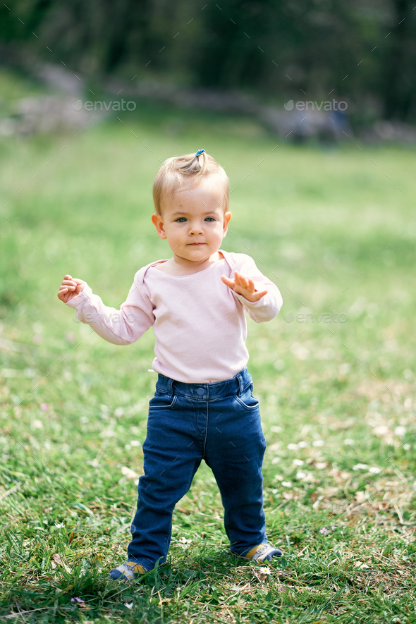 Little funny girl walking in a green meadow Stock Photo by Nadtochii