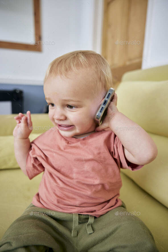 Toddler holding smart phone with animated expression indoors - Stock Photo - Images