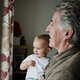Close up of smiling toddler in arms of grandfather looking out of window - PhotoDune Item for Sale