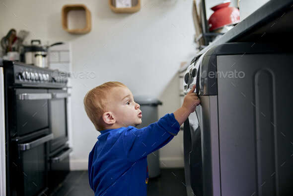 Toddler reaching up and touching appliance in kitchen - Stock Photo - Images