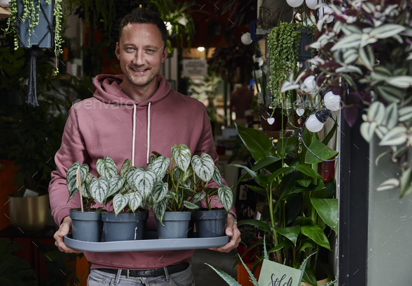 Portrait of man holding tray of plants in doorway of flower shop - Stock Photo - Images
