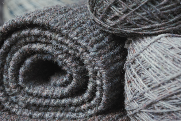 Rolled gray knitted scarf and skein of yarn. Woolen hand-knitted product.