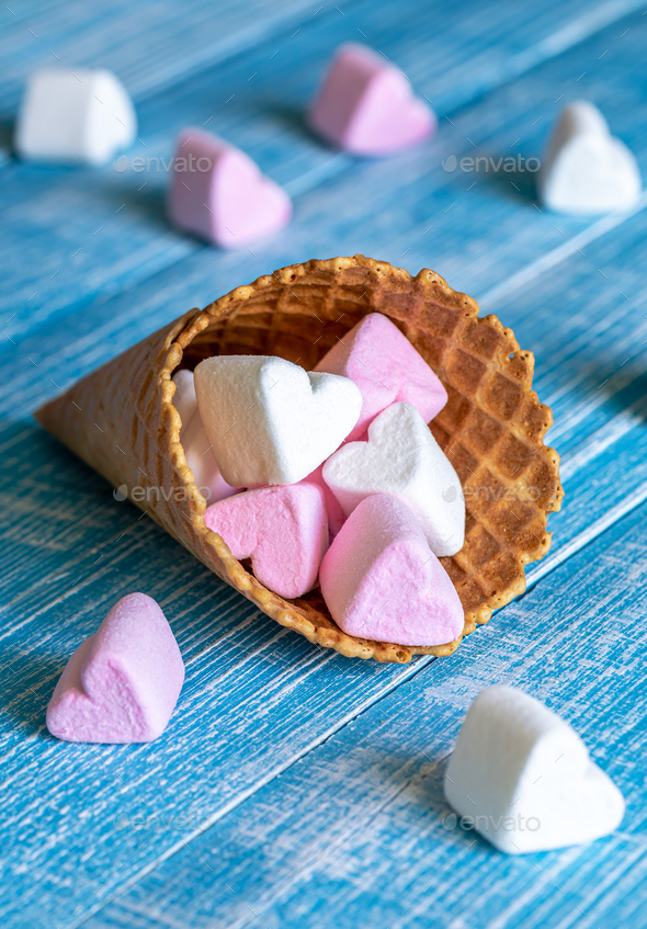 Waffle cone with heart-shaped marshmallows, close-up on a blue