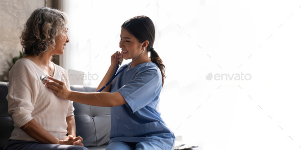 Young nurse listening to older woman lung or heart sound with stethoscope