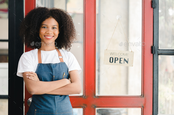 A young American woman stands in front of a restaurant door with an open sign, she is a waitress of