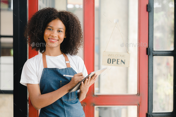 A young American woman stands in front of a restaurant door with an open sign, she is a waitress of