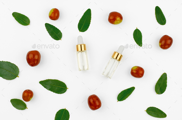 Jojoba oil in a transparent bottle with a dropper and fresh jojoba fruit on a white background