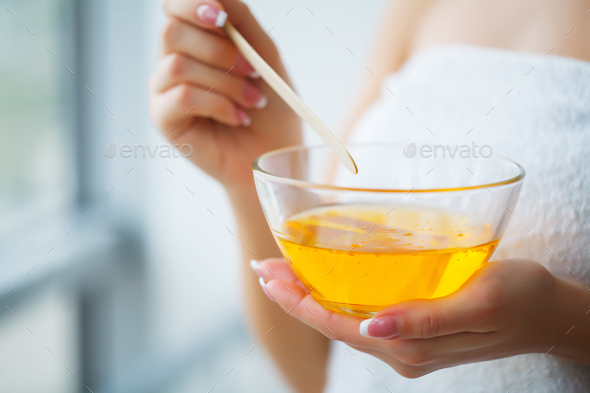 Female hand and orange paraffin wax in bowl.