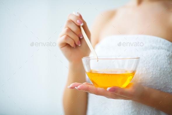 Female hand and orange paraffin wax in bowl.
