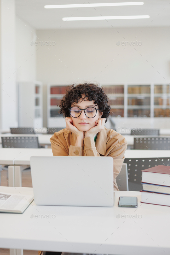 thoughtful woman works in library, watches an educational webinar on Internet, is bored. coworking - Stock Photo - Images