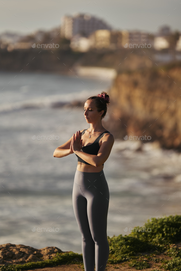 Woman standing a grateful namaste yoga pose on the beach next to the ocean  in cloudy weather. Zen, meditation, peace. Stock Photo by ©Fesenko 117056712