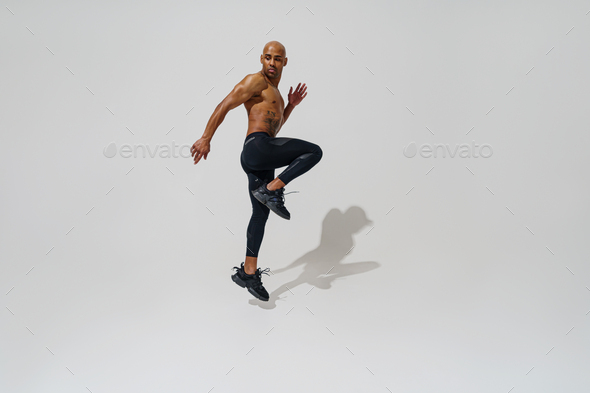 Active sporty man with naked torso jumping on white studio